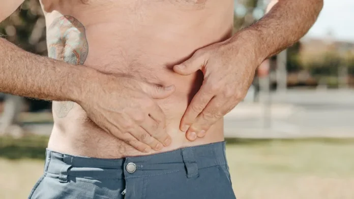 A tattooed, topless man touching his stomach outdoors, focusing on body awareness and self-care.