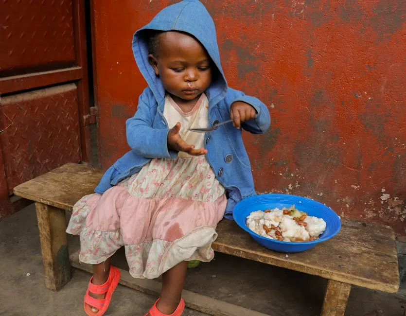 Cute child in blue hoodie enjoying a meal on a wooden bench, showing innocence and contentment.