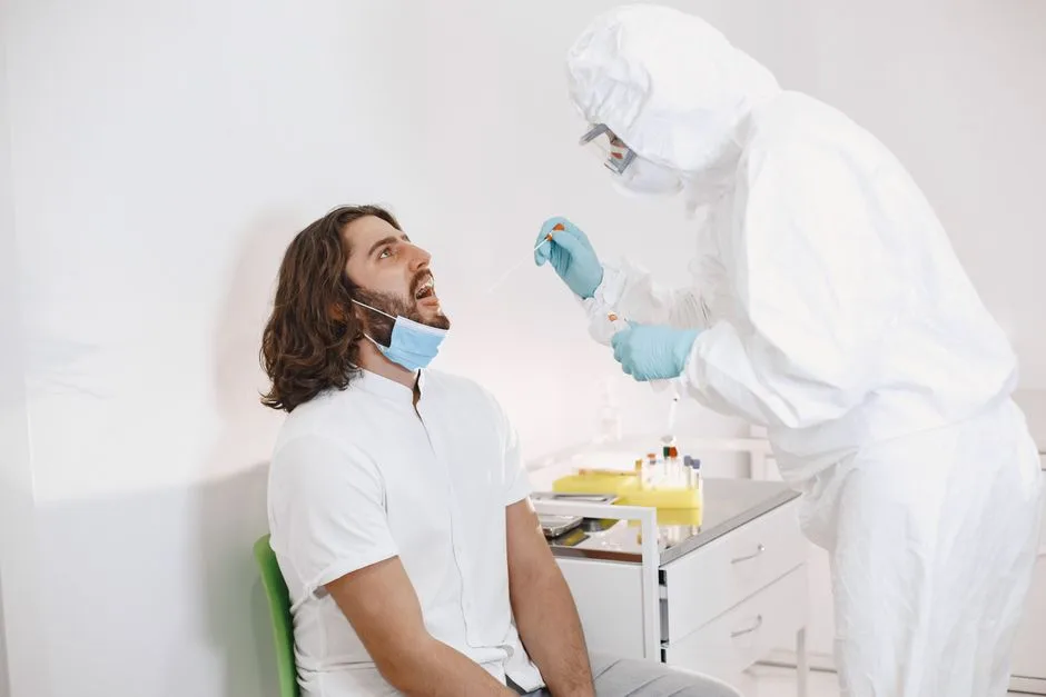 Healthcare worker in protective gear swabbing a man for COVID-19 indoors.